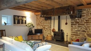 A rustic living room with stone walls, a fireplace, and a television on a wooden cabinet. - "Le Cerisier" Holiday Cottages, Champsecret (Champsecret)