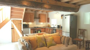 A cozy kitchen with wooden cabinets, a dining area with a sofa and cushions, and a staircase leading to an upper level. - "Le Cerisier" Holiday Cottages, Champsecret (Champsecret)