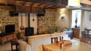 A cozy living room with a stone wall, wooden furniture, a fireplace, and a television. - "Le Cerisier" Holiday Cottages, Champsecret (Champsecret)