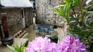 A stone building with a tiled roof, a metal table and chairs, and a small garden area with flowers. - "Le Cerisier" Holiday Cottages, Champsecret (Champsecret)