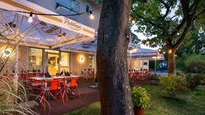 An outdoor dining area with tables and chairs, string lights, and a tree. - Kristallhotel Fettehenne (Leverkusen)