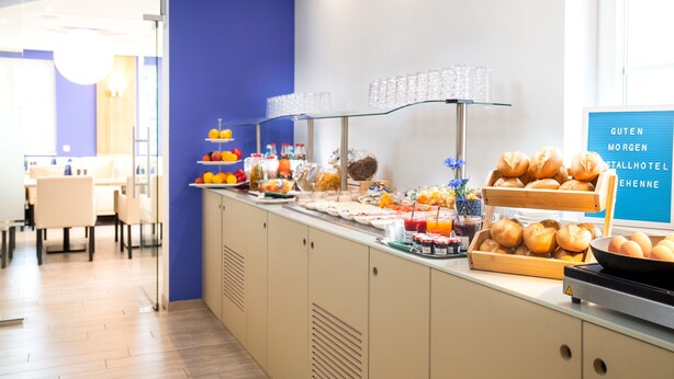 A buffet with various food items and drinks, a sign with text, and a seating area in the background. - Kristallhotel Fettehenne (Leverkusen)