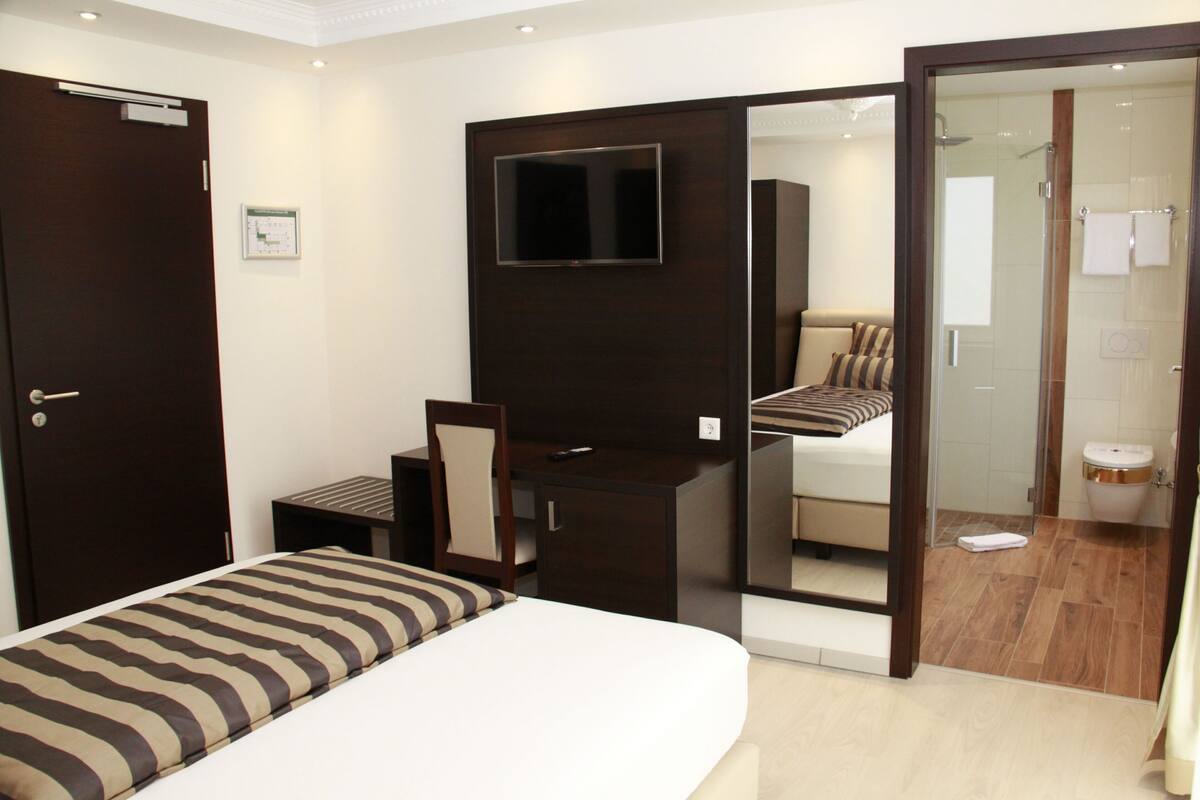A hotel room with a bed, a desk, a TV, a shower, and a bathroom.