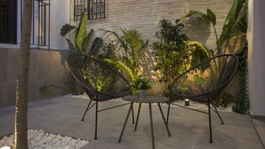 Un espace patio aménagé avec deux chaises en fil de fer noir, une petite table ronde et diverses plantes.