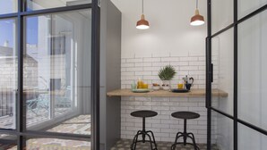 Une cuisine moderne avec une porte vitrée donnant sur un balcon, deux tabourets et un coin repas pour le petit-déjeuner.