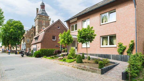 A street with traditional brick buildings, a church tower, and a paved walkway with trimmed bushes. - Hotel am Tiergarten (Raesfeld)