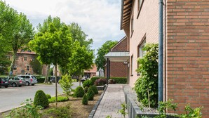 A brick building with a paved walkway and landscaped garden. - Hotel am Tiergarten (Raesfeld)