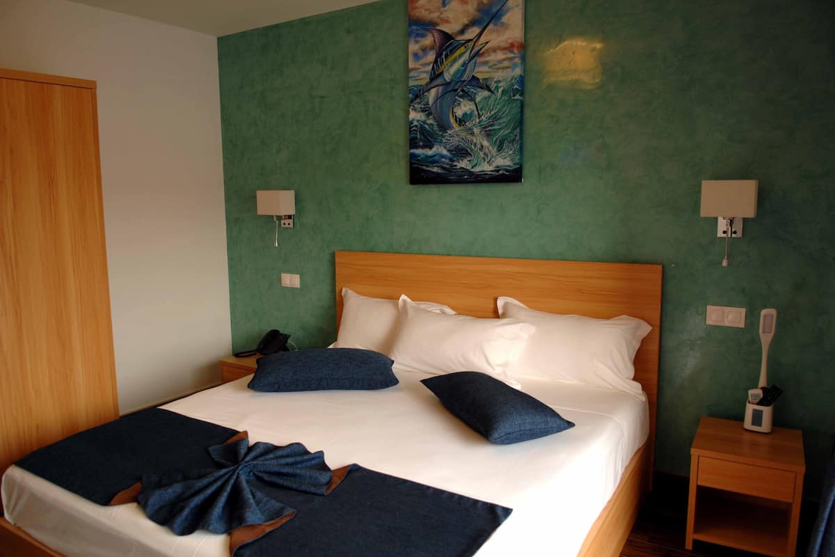 Un lit bien fait, avec une literie blanche et bleu foncé, une tête de lit en bois et un tableau représentant un poisson accroché au mur.