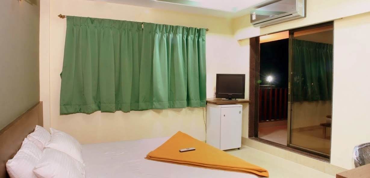 Hotelkamer met een bed, een klein bureau, een televisie en een glazen schuifdeur naar een buitenruimte.