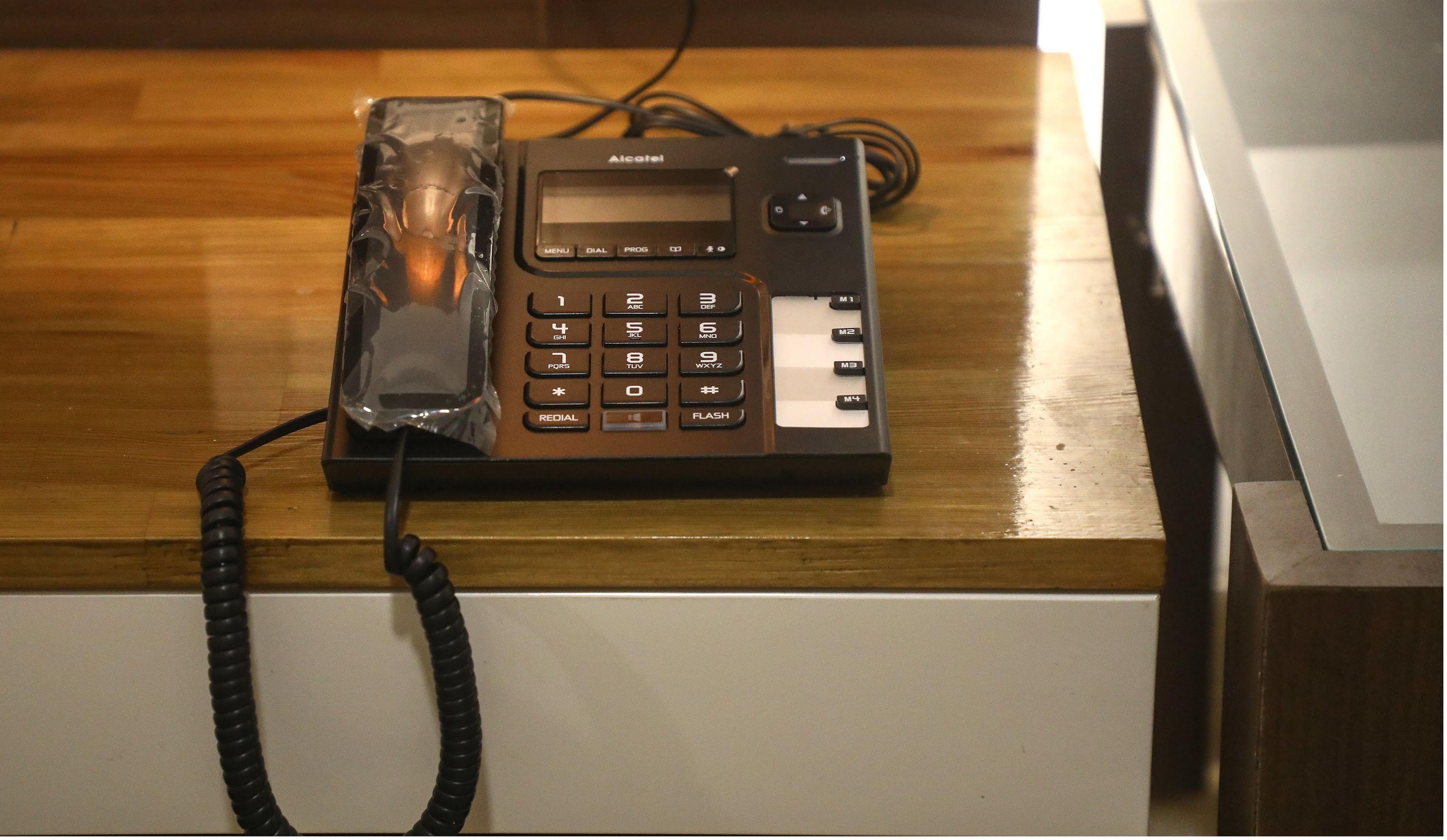 En brun bordstelefon från Alcatel med knappsats och en liten skärm, ansluten med en spiralformad sladd.