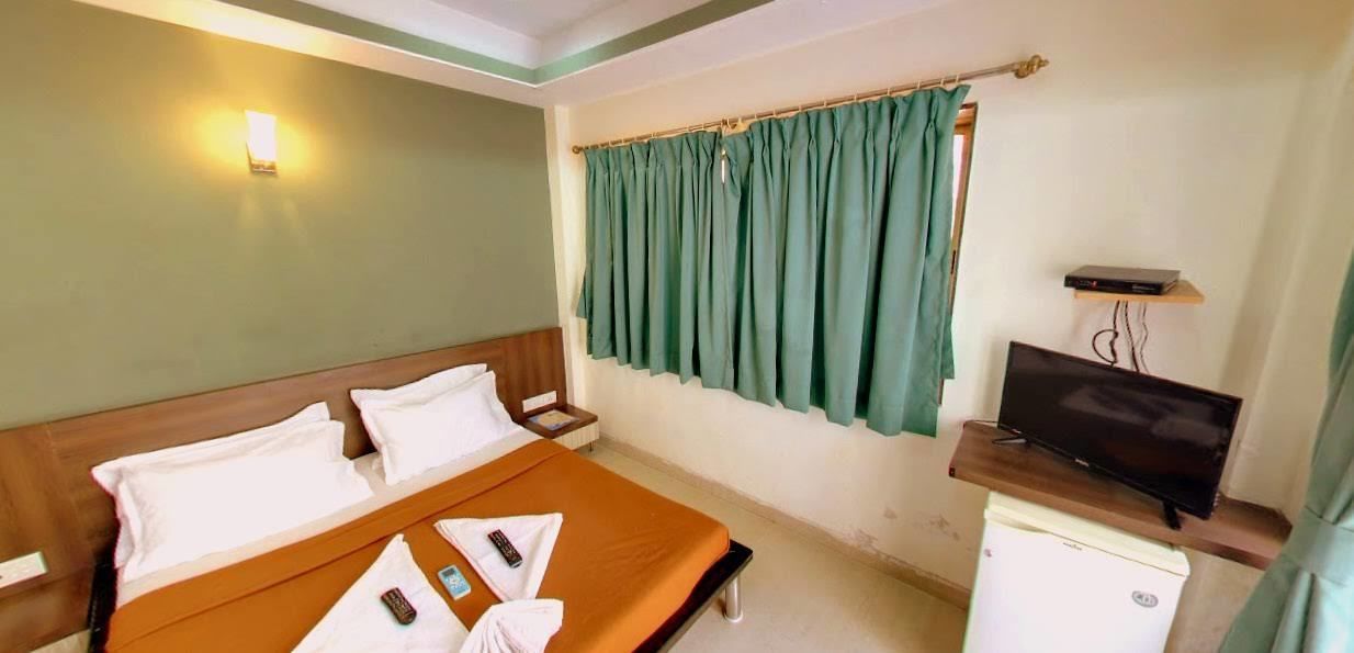 Una habitación de hotel con cama, televisor, refrigerador pequeño y ventana con cortinas.