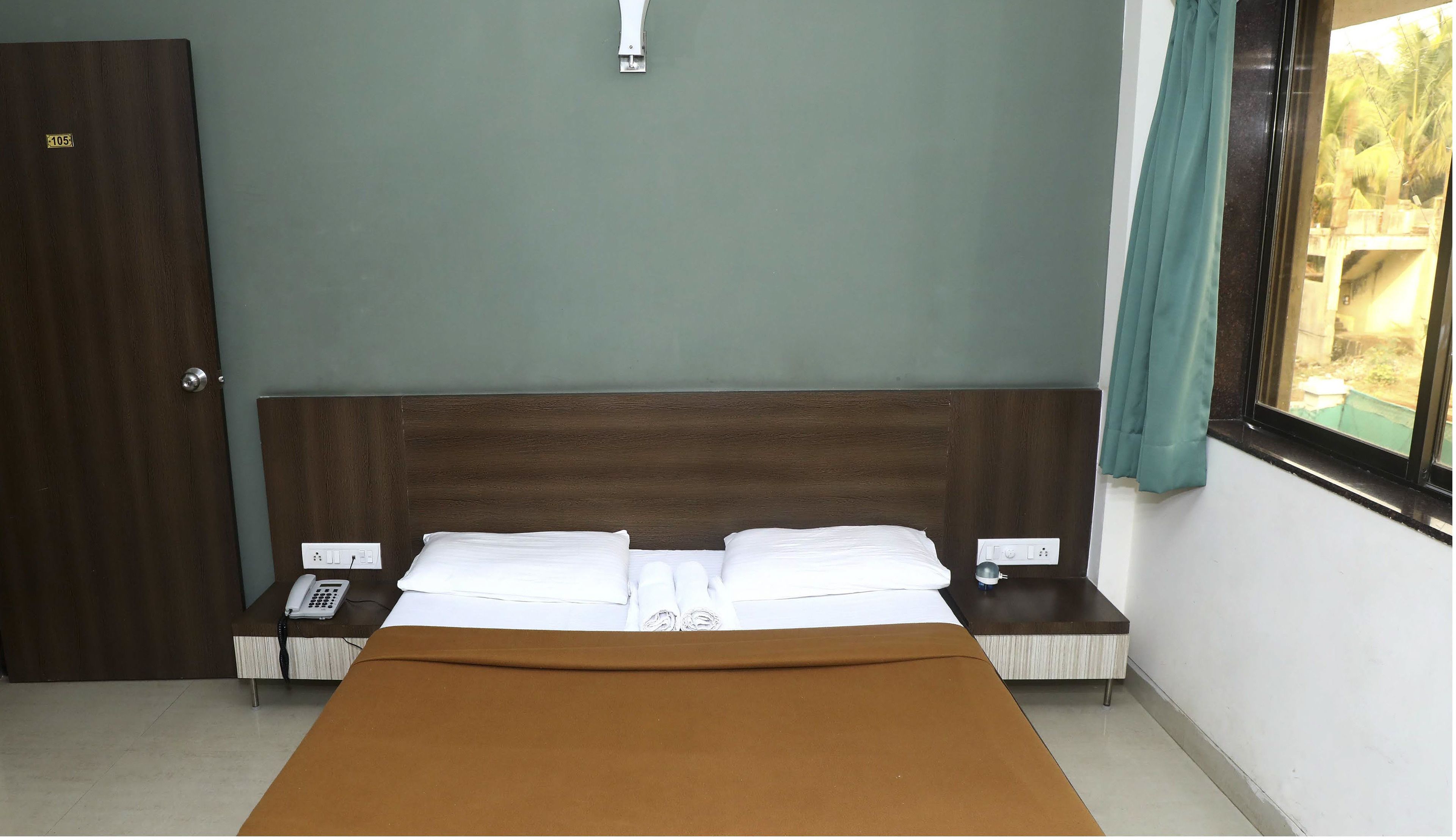A hotel room with a bed, a bedside table, a telephone, and a window with curtains.