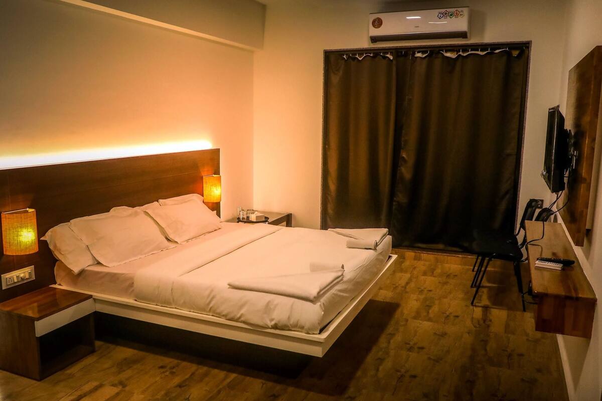 A hotel room with a bed, bedside lamps, a TV, and a wooden floor.