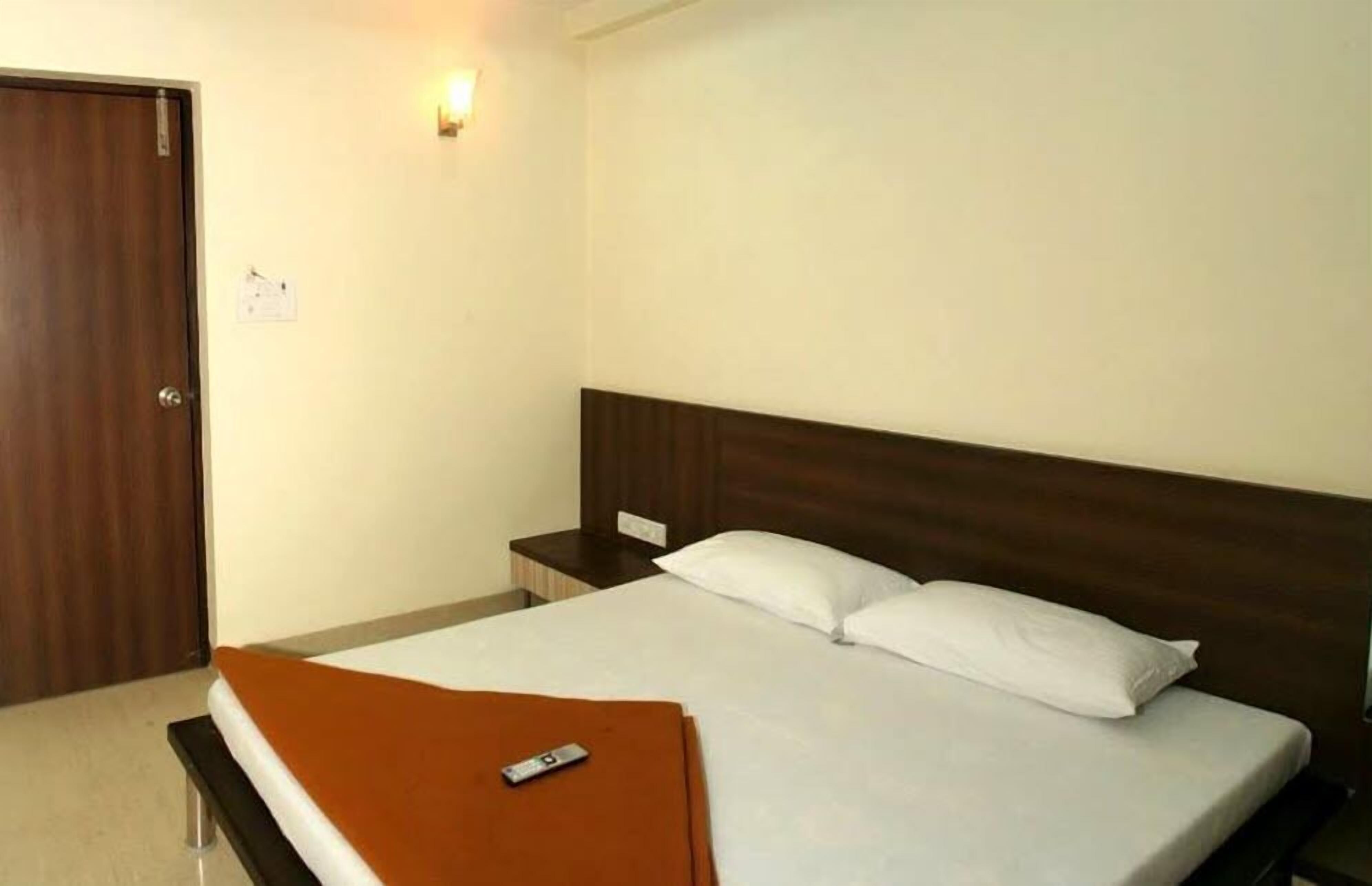A hotel room with a single bed, a wooden headboard, a nightstand, and a wall-mounted light.
