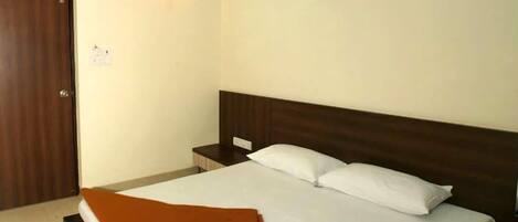 A hotel room with a single bed, a wooden headboard, a nightstand, and a wall-mounted light.