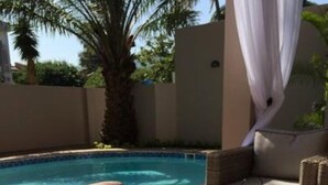 A poolside area with a small hot tub, wicker furniture, and a white curtain. - MyGuest (Maputo)
