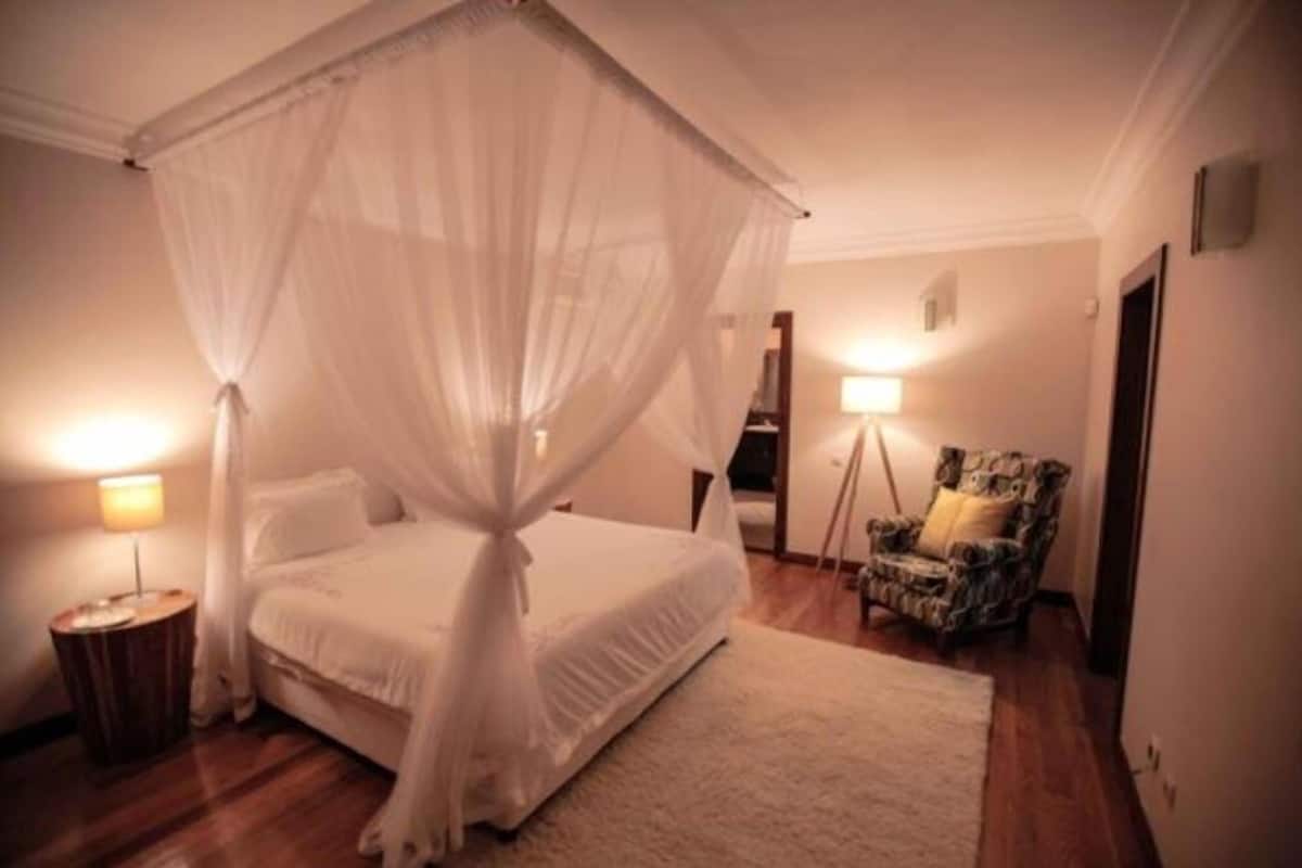 A bedroom with a four-poster bed, a bedside lamp, a chair, and a small table.