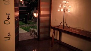 A dimly lit hallway with a decorative floor lamp, a staircase, and a door leading to an outdoor area with flowers. - MyGuest (Maputo)
