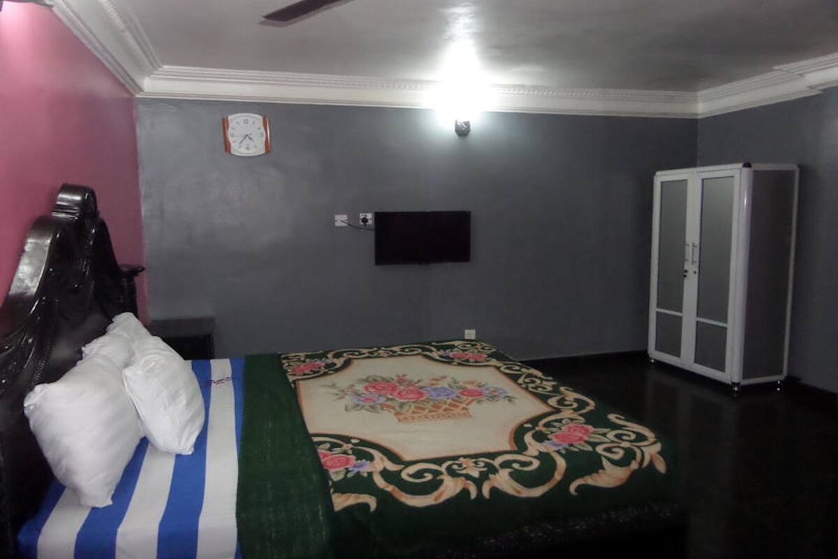Un dormitorio con cama, armario, reloj y televisor de pantalla plana en la pared.