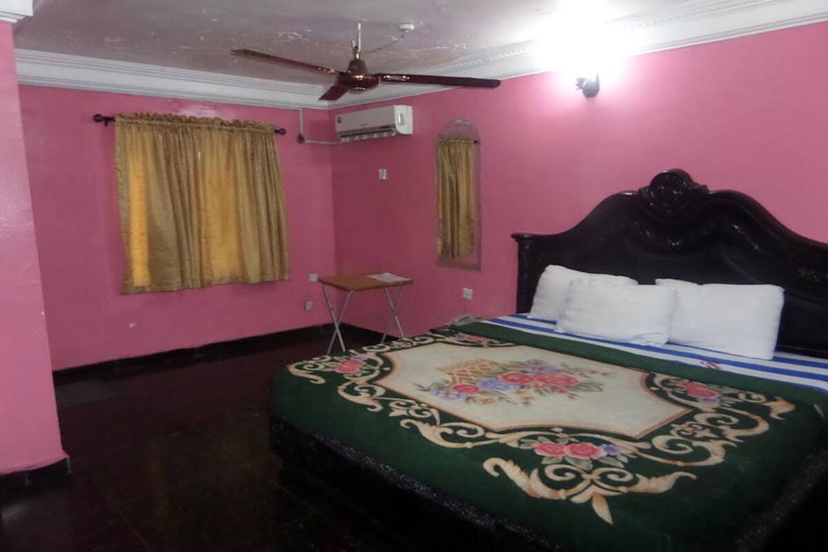 Una habitación con cama, ventilador de techo, aire acondicionado y una mesita.