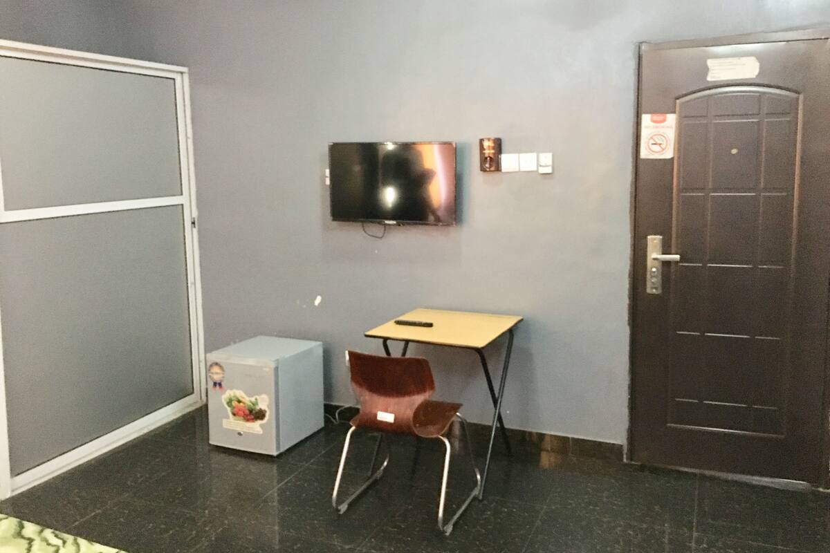Una habitación pequeña con escritorio, silla y televisor fijado a la pared.