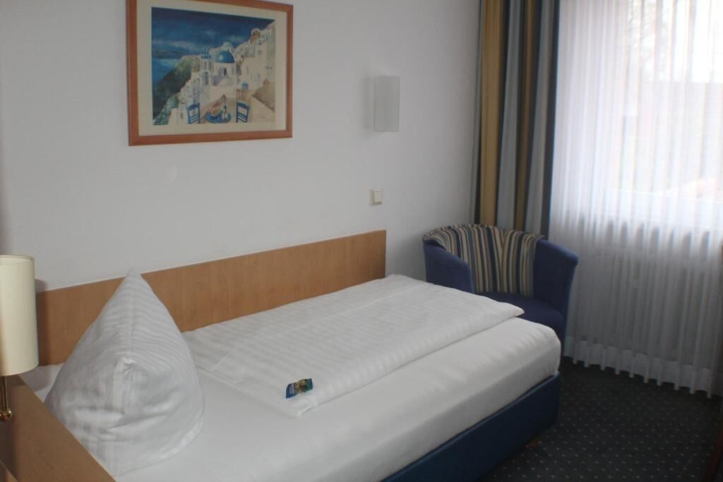 A hotel room with a bed, a chair, a lamp, and a painting on the wall.