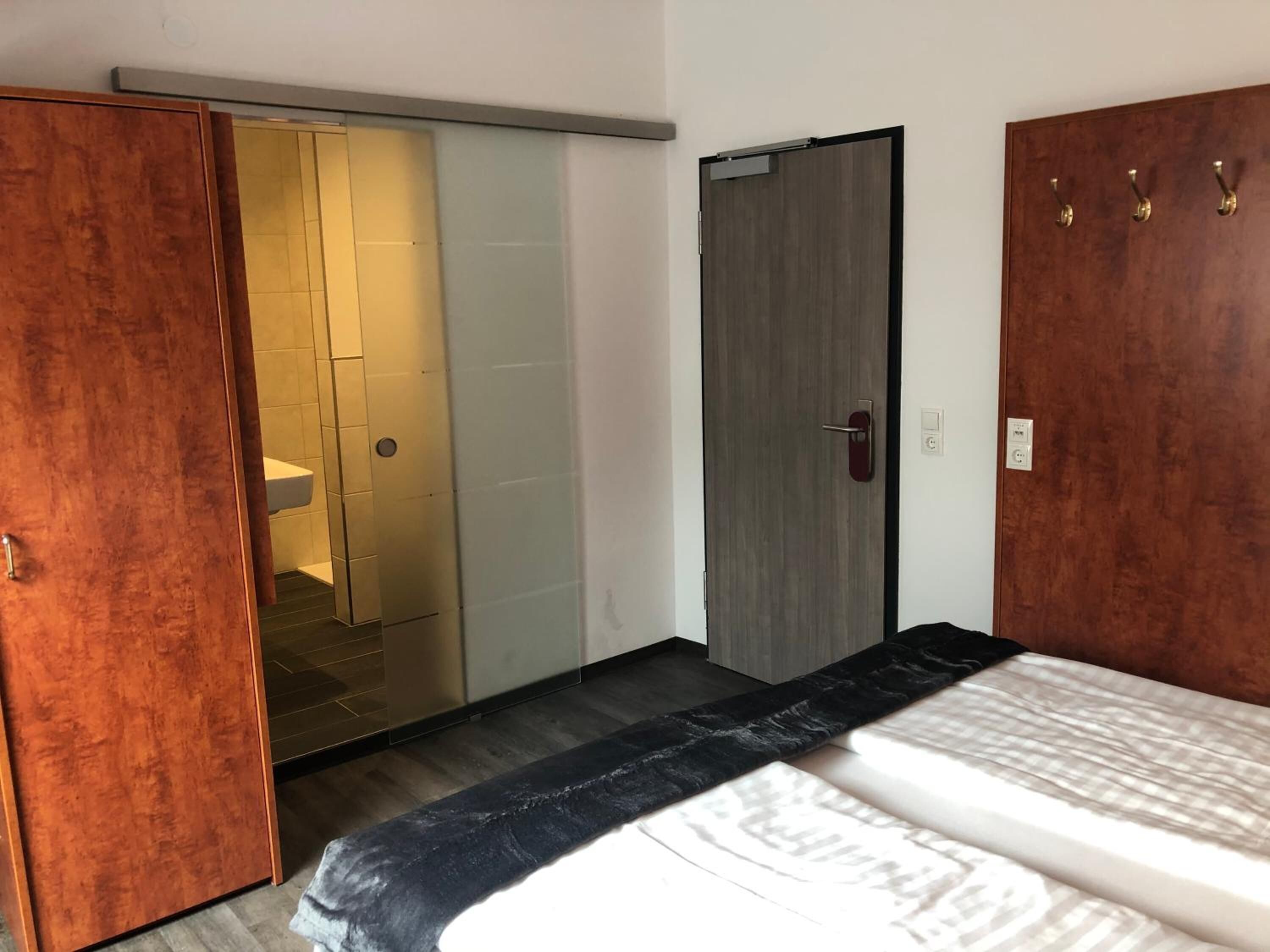 Une chambre à coucher comprenant un lit, une armoire, une porte et une salle de bain visible à travers une porte en verre.
