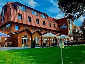 A hotel with a brick facade, outdoor seating with umbrellas, and a clear sky. - Hotel Am Stadtpark (Papenburg)