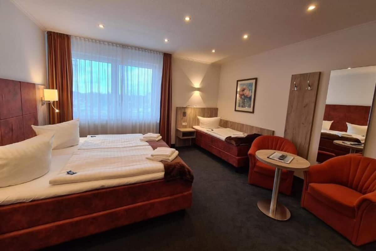 A hotel room with a large bed, a smaller bed, a sofa, a chair, and a small table.