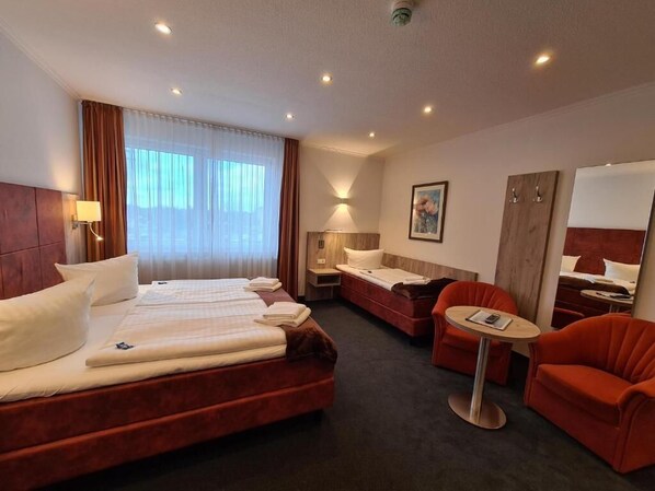 Una habitación de hotel con una cama grande, una cama más pequeña, un sofá, una silla y una mesita.