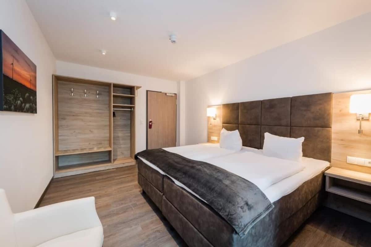 A modern hotel room with a large bed, a wardrobe, and a bedside table.