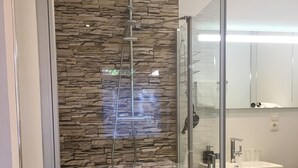 A modern bathroom with a stone wall, a glass-enclosed shower, and a sink with a mirror above it. - Hotel Am Stadtpark (Papenburg)