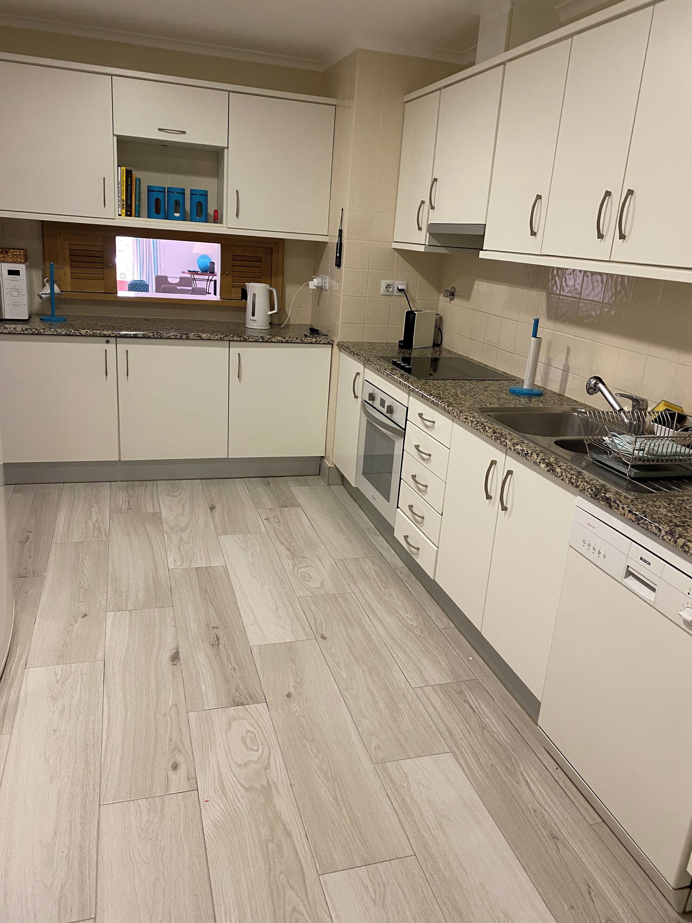 Una cocina moderna con armarios blancos, encimera de granito, lavavajillas Bosch y suelo de madera.