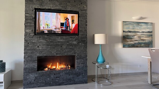 A modern living room with a stone fireplace, a flat-screen TV mounted above it, a glass table with a teal vase, and a painting on the wall. - Luxury, spacious, two bedroom apartment on the Vill Sol Golf & Spa Resort (Quarteria)