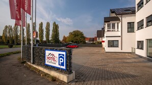 L’entrée d’un hôtel, avec un panneau indiquant un espace de stationnement, une voiture rouge garée sur le parking, et un bâtiment moderne doté de panneaux solaires.