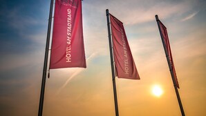 Trois drapeaux sur lesquels on peut lire « HOTEL AM STADTRAND », avec un ciel de coucher de soleil en arrière-plan.