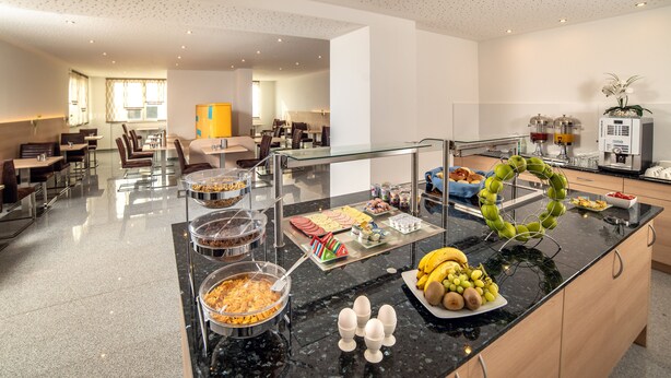 Un espace de restauration d’hôtel comprenant des buffets, des tables et des chaises, ainsi qu’une cuisine.