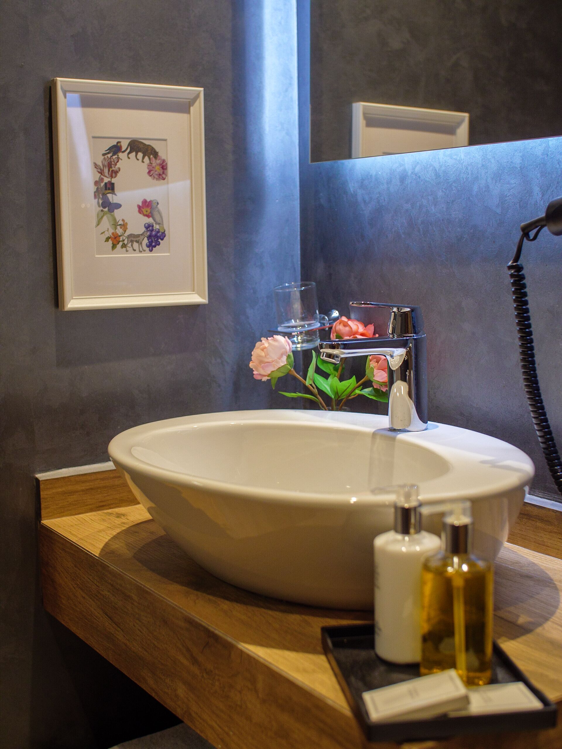 Une salle de bain avec un grand lavabo blanc, une œuvre d’art florale encadrée, un récipient en verre et un téléphone.