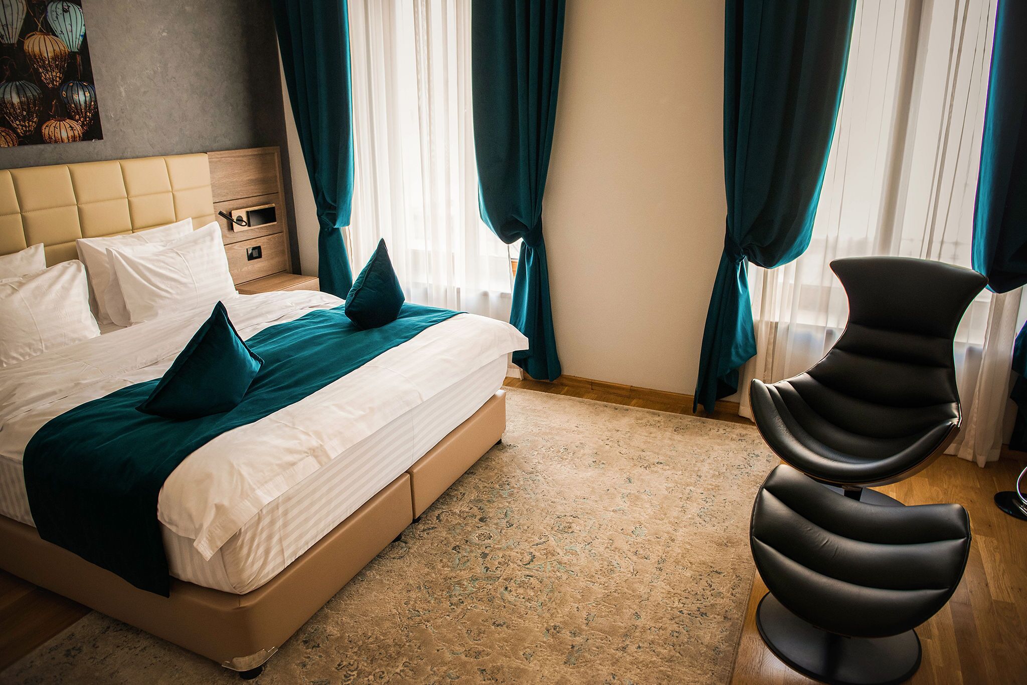 Habitación de hotel con cama, mesita de noche, una silla y un ventanal con cortinas.