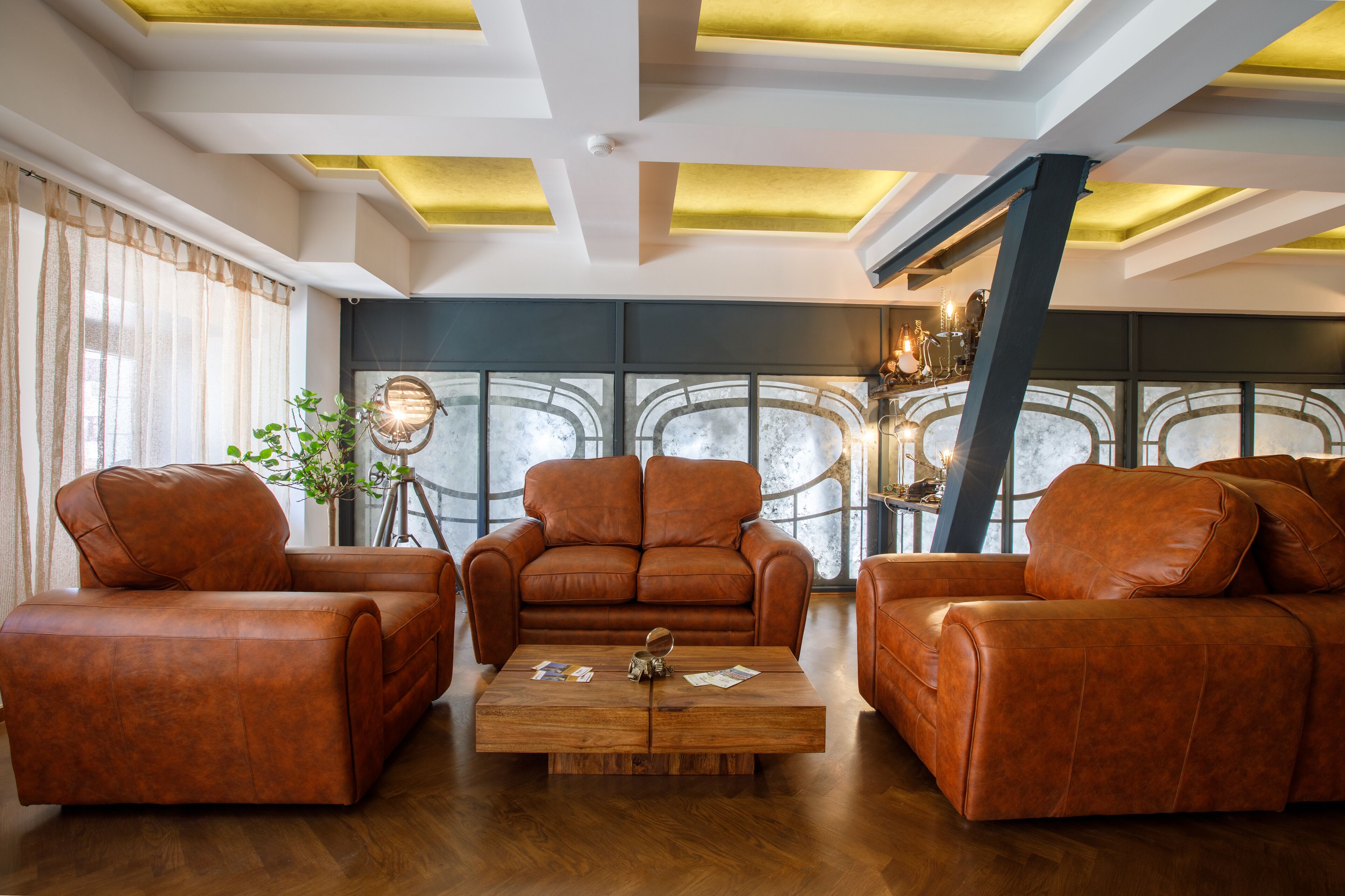 Una sala de estar moderna con sofás de cuero, una mesa de centro de madera y ventanas grandes con paneles decorativos de vidrio.