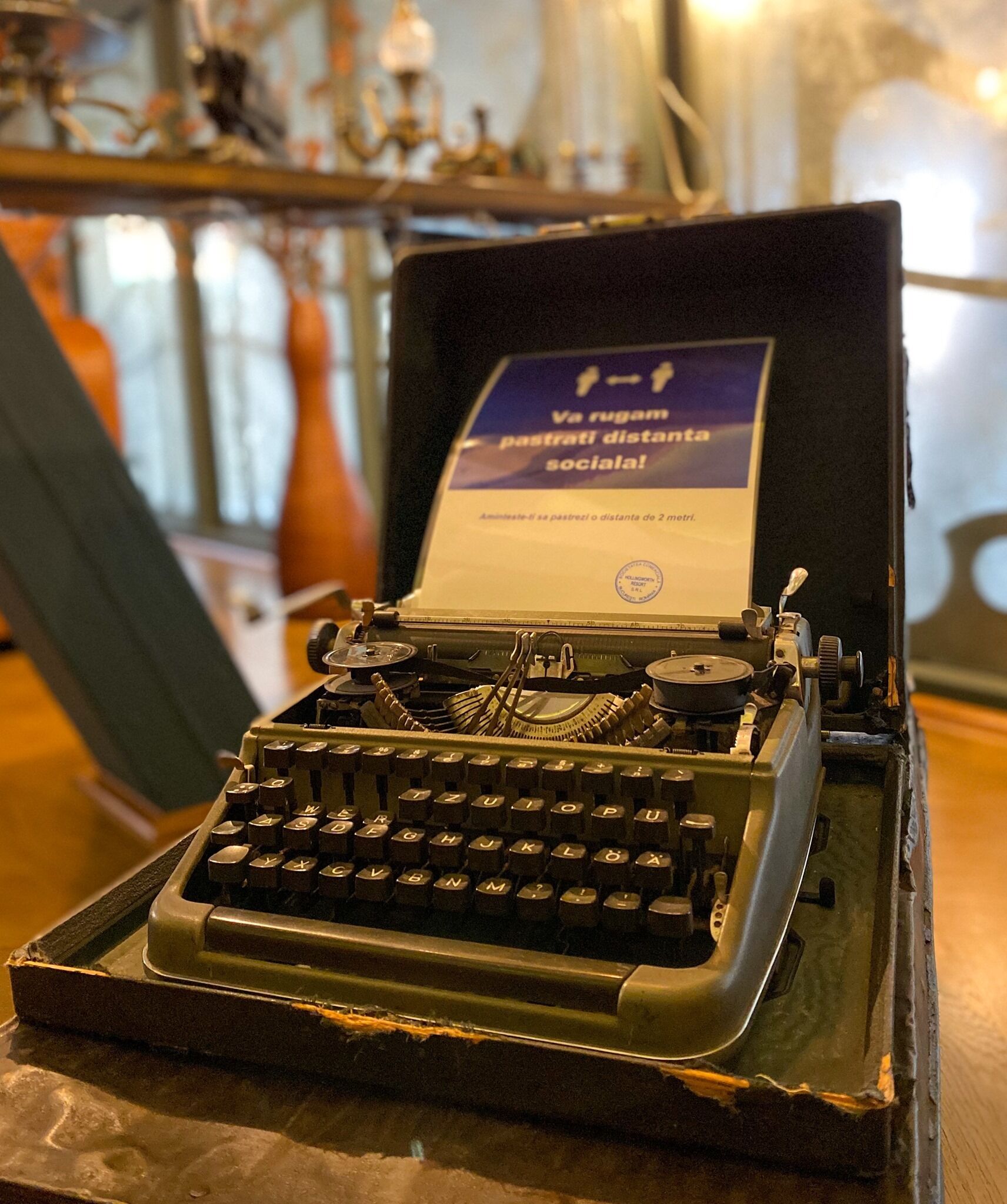 An old-fashioned typewriter with a sign in a foreign language, placed on a wooden surface.