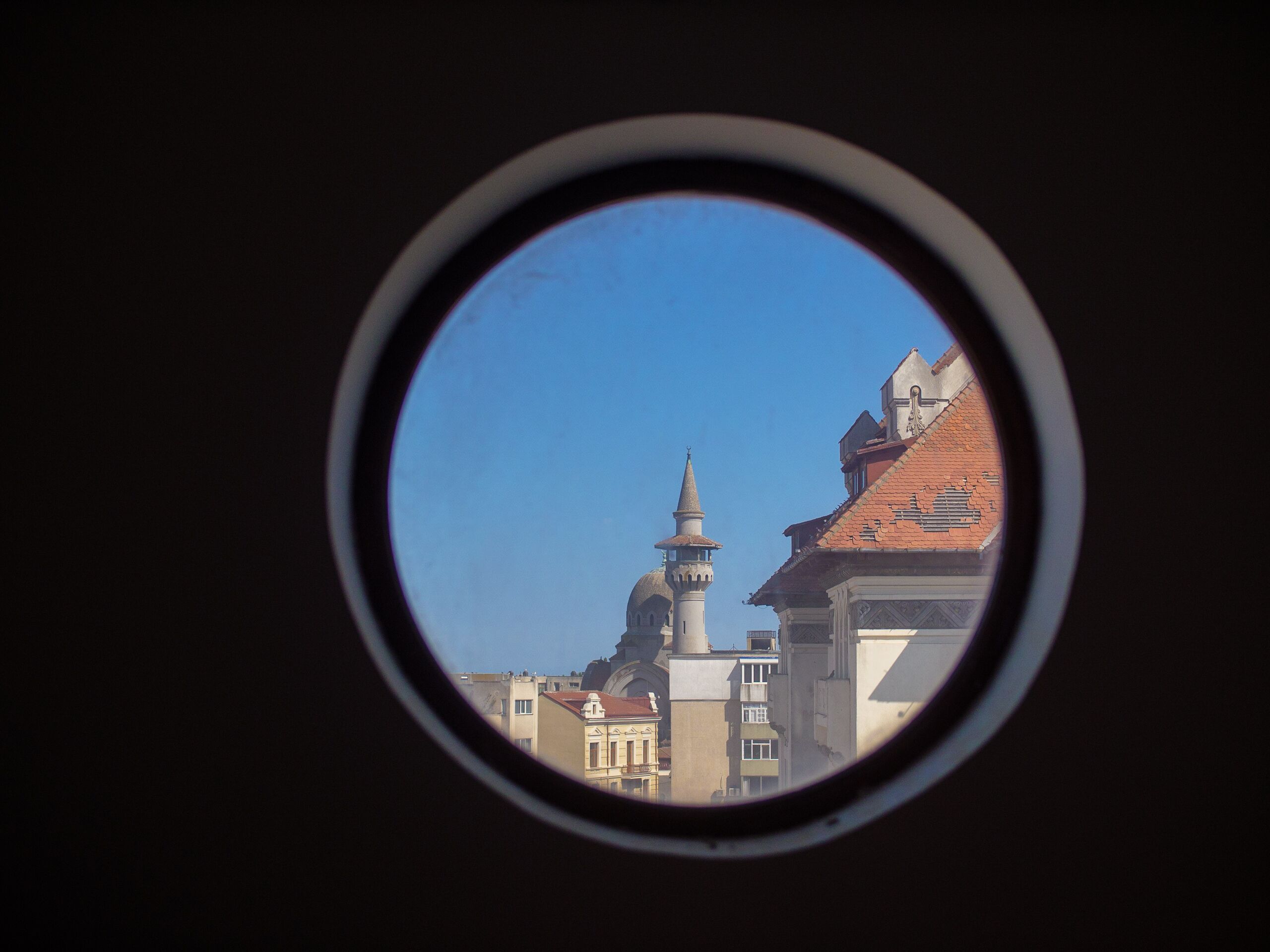A view through a circular window of a building with a prominent tower and dome, suggesting historical architecture.