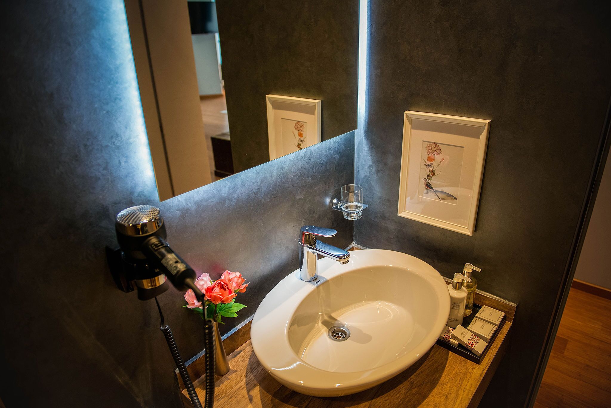 Un baño con lavamanos, espejo, secador de pelo y un florero con flores.