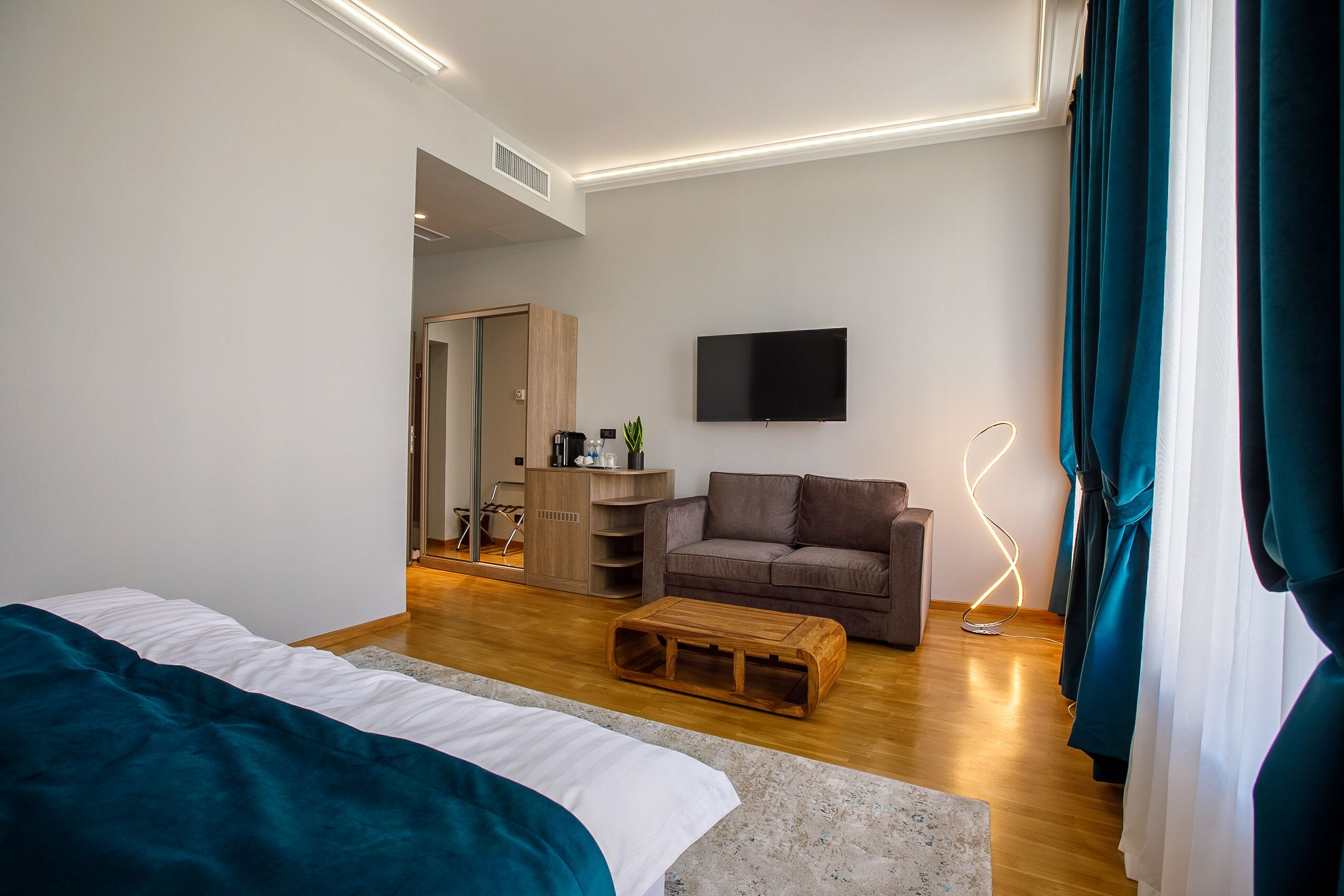 Une chambre d’hôtel moderne équipée d’un lit, d’un canapé, d’une télévision et d’une table basse en bois.