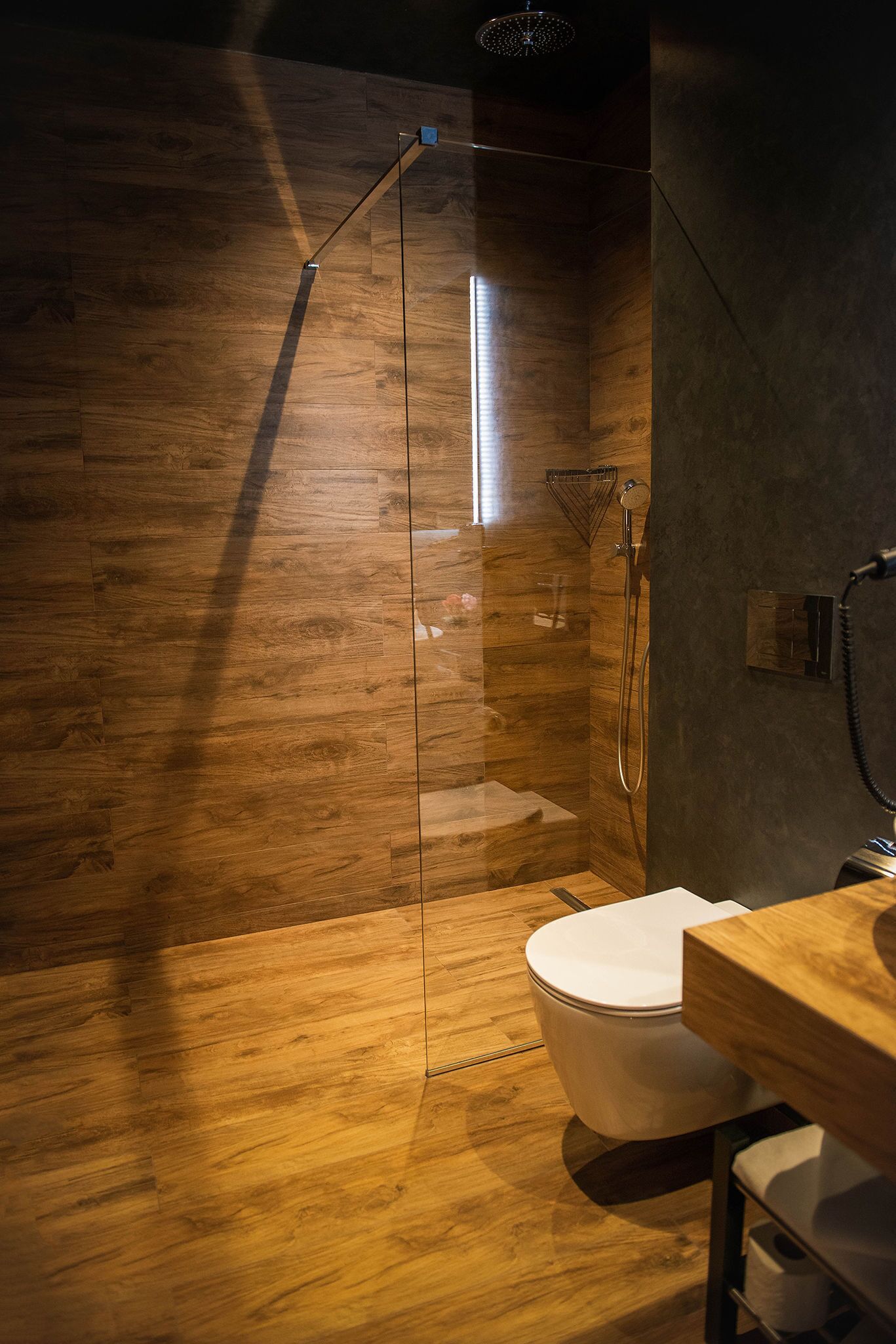 A modern bathroom with a wooden floor, a glass-enclosed shower, and a white toilet.