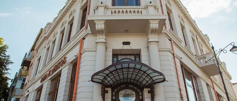 Un edificio histórico con una entrada imponente, amplias escaleras y un llamativo letrero con las letras 'CH'.