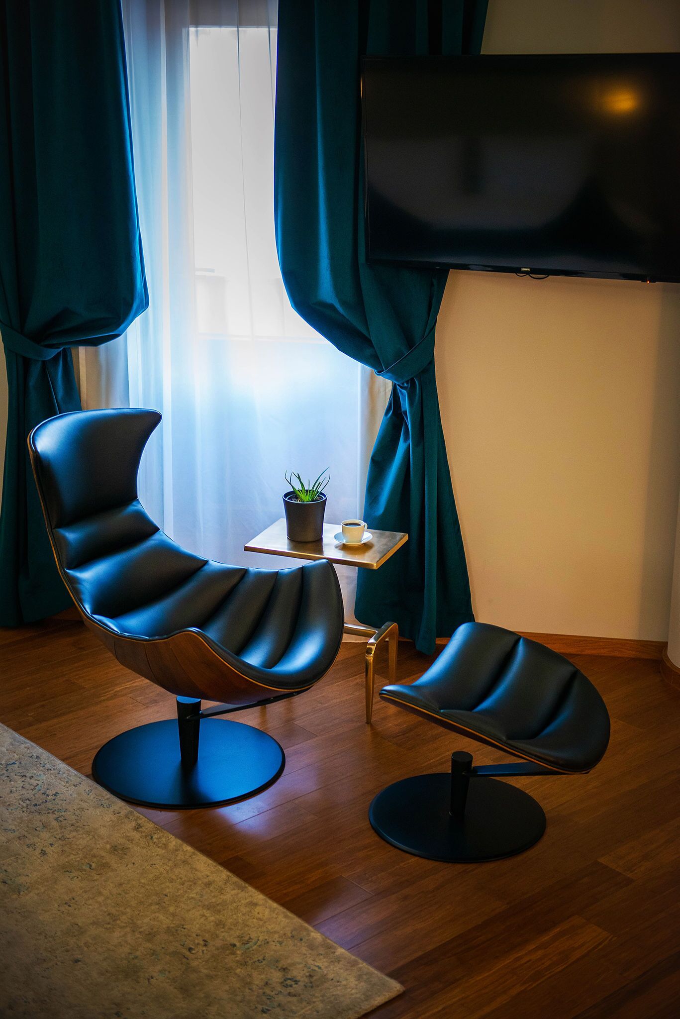 Ein modernes Wohnzimmer mit zwei schwarzen Ledersesseln, einem kleinen Tisch mit Pflanze und Tasse sowie einem an der Wand befestigten Fernseher.