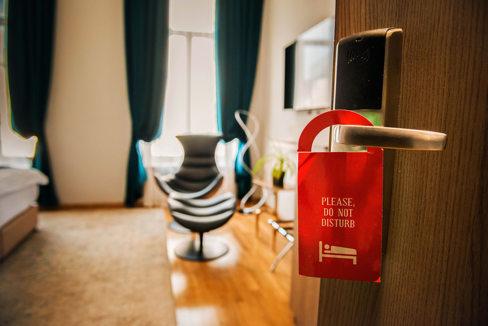 A hotel room with a red sign on the door, a chair, and a bed.