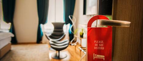 A hotel room with a red sign on the door, a chair, and a bed.
