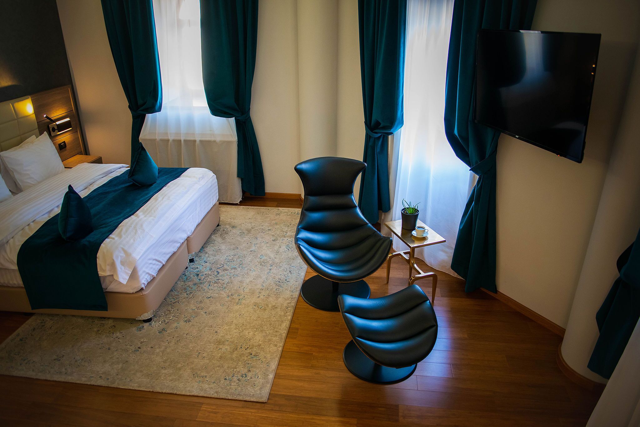 A hotel room with a bed, a TV mounted on the wall, and two modern chairs.